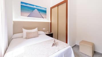 A hotel room with a bed, a nightstand, a wooden wardrobe, and a painting of a beach.