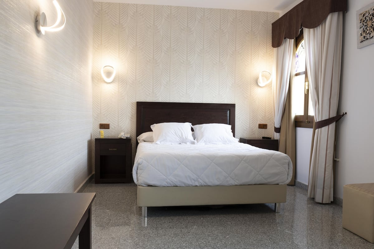 A neatly arranged bedroom with a bed, bedside tables, and wall sconces.