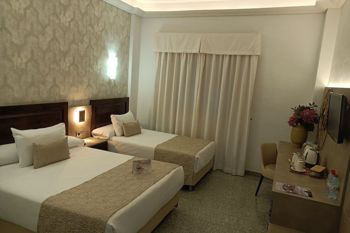 A hotel room with two beds, a desk, a chair, a TV, and a window with curtains.