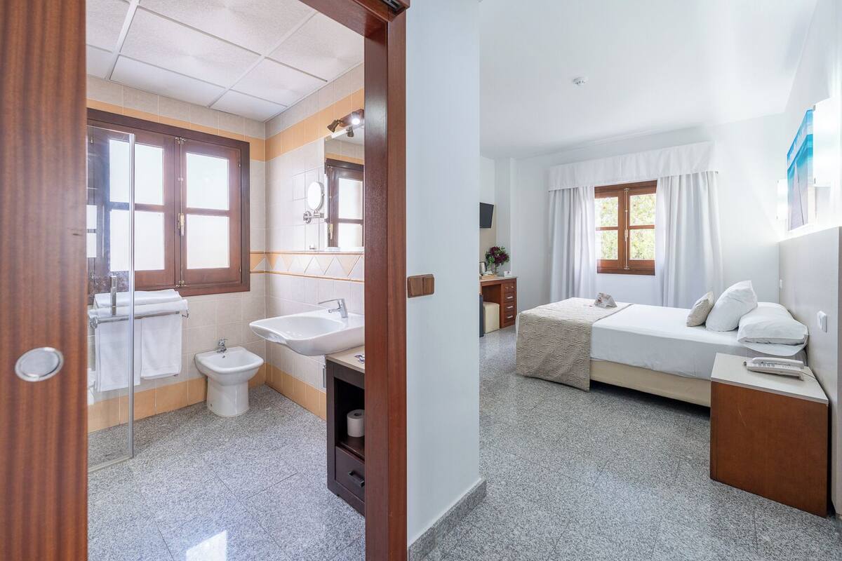 A hotel room with a bathroom, a bed, a desk, and a window.