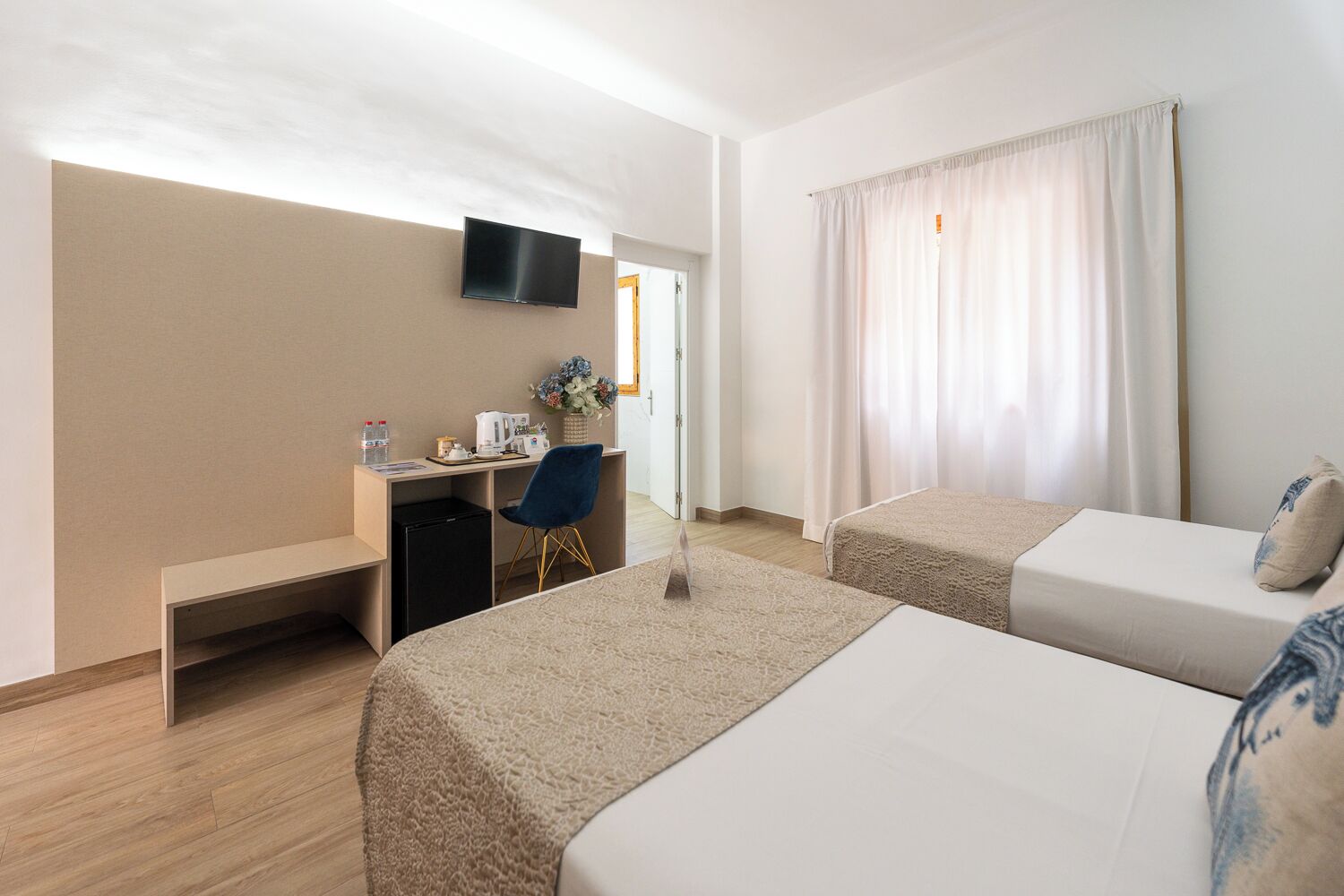 Een hotelkamer met twee bedden, een bureau met stoel, een televisie en een raam met gordijnen.