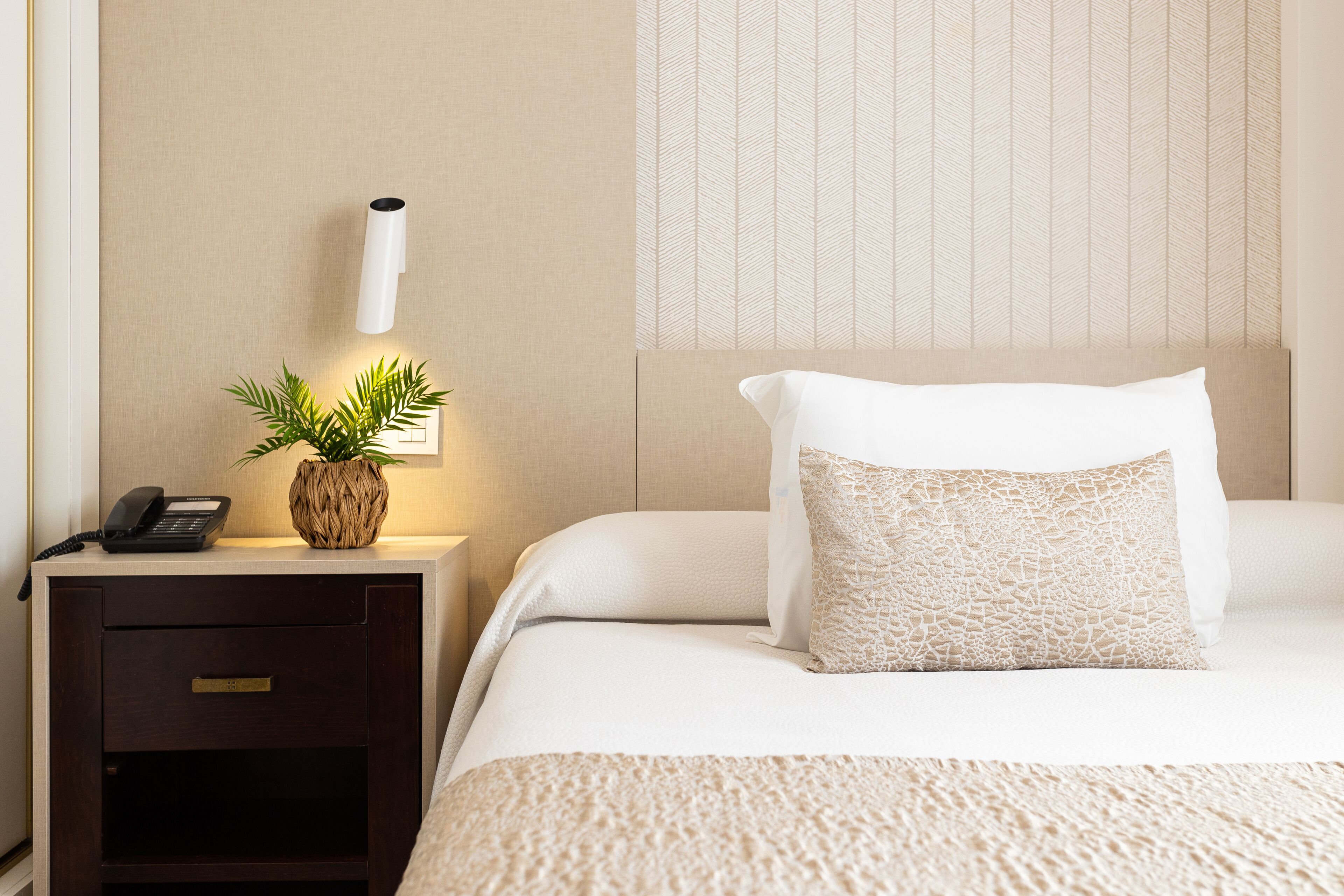 Une chambre d’hôtel bien rangée, avec un lit, une table de chevet dotée d’une lampe, un téléphone et une plante décorative.
