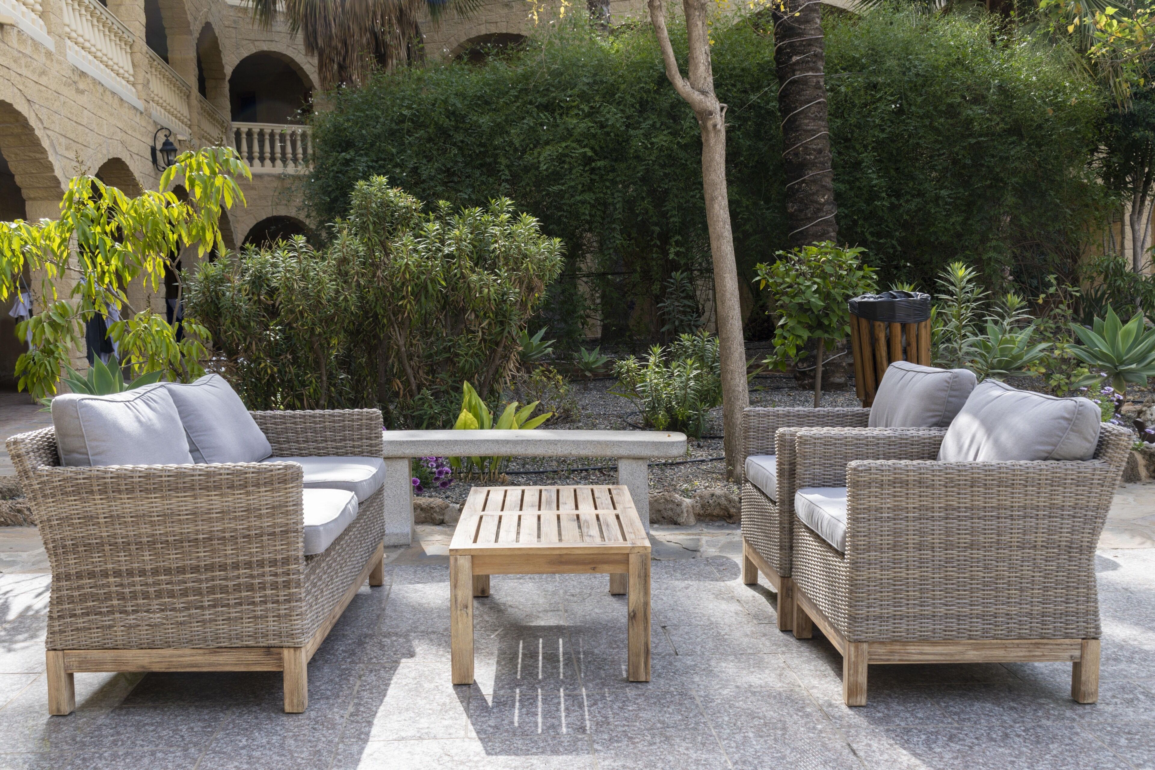 A courtyard with wicker furniture, a stone table, and lush greenery.