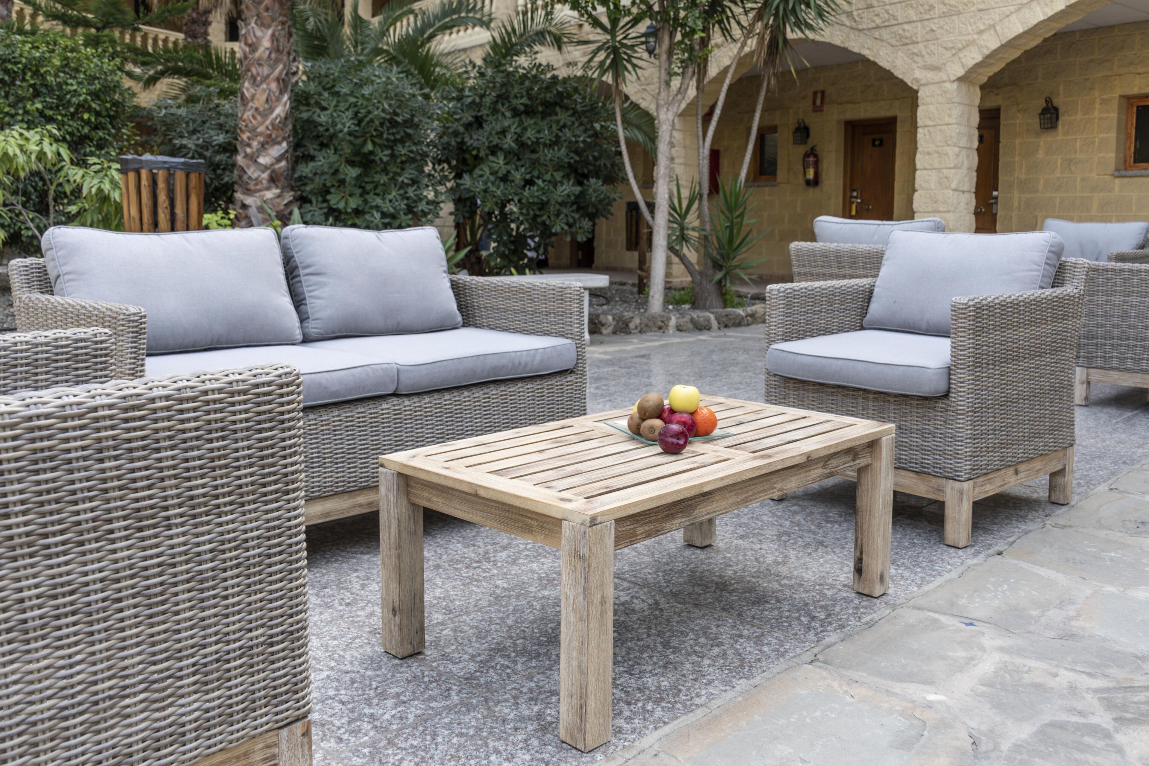 Ein Patio mit Korbmöbeln, einem Holztisch mit Früchten und einem Steinboden.