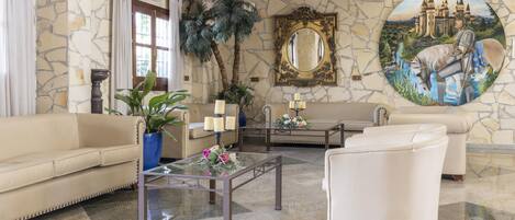 A lobby with a stone wall, a large mirror, a painting of a knight and horse, a sofa, a coffee table, and a potted plant.