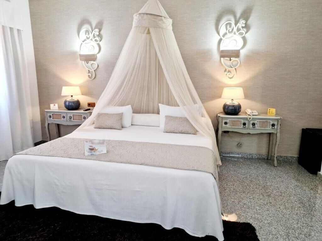 A bedroom with a canopy bed, bedside lamps, and a nightstand with a lamp.