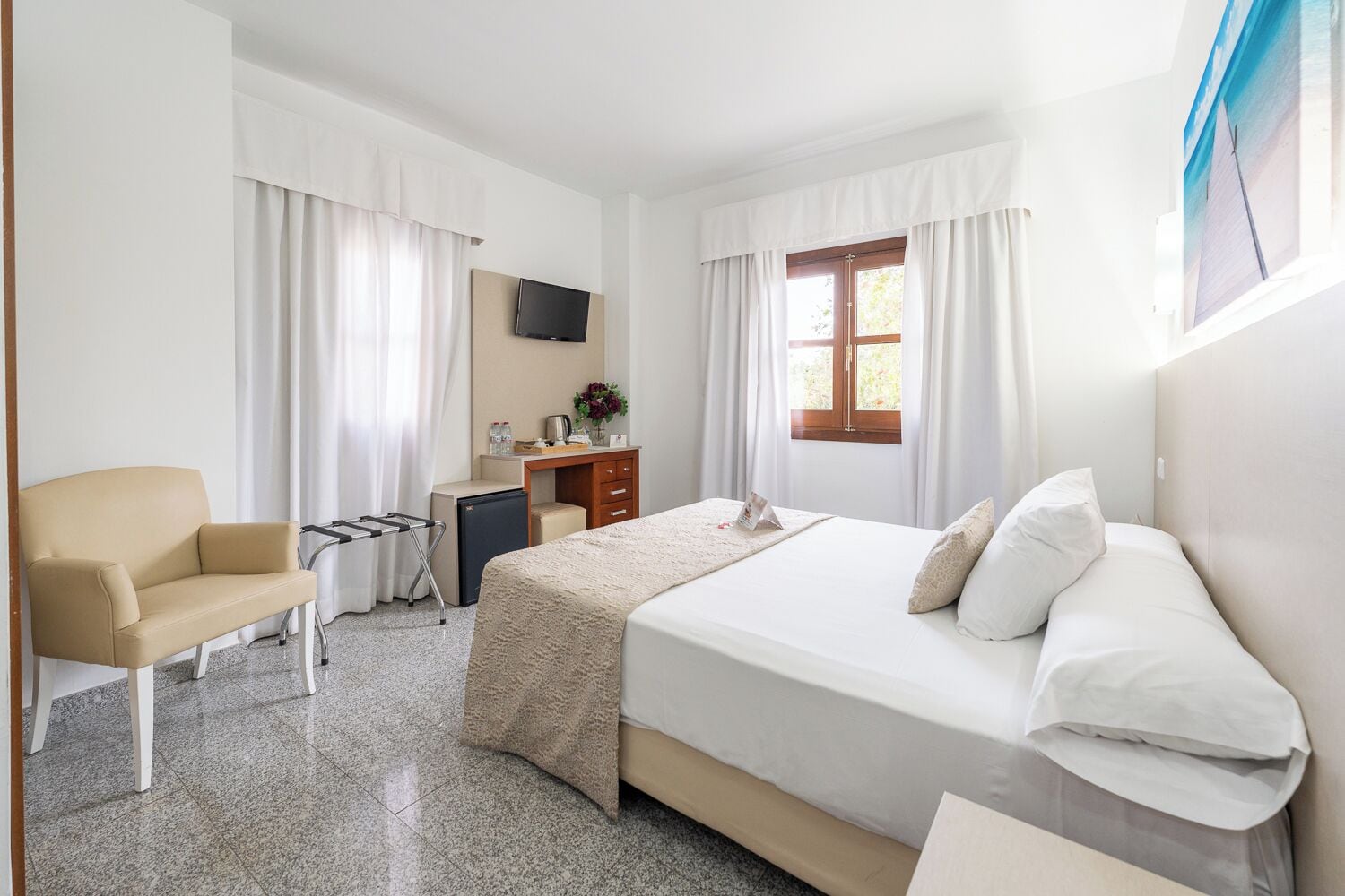 A hotel room with a bed, a desk, a chair, a TV, and a window.