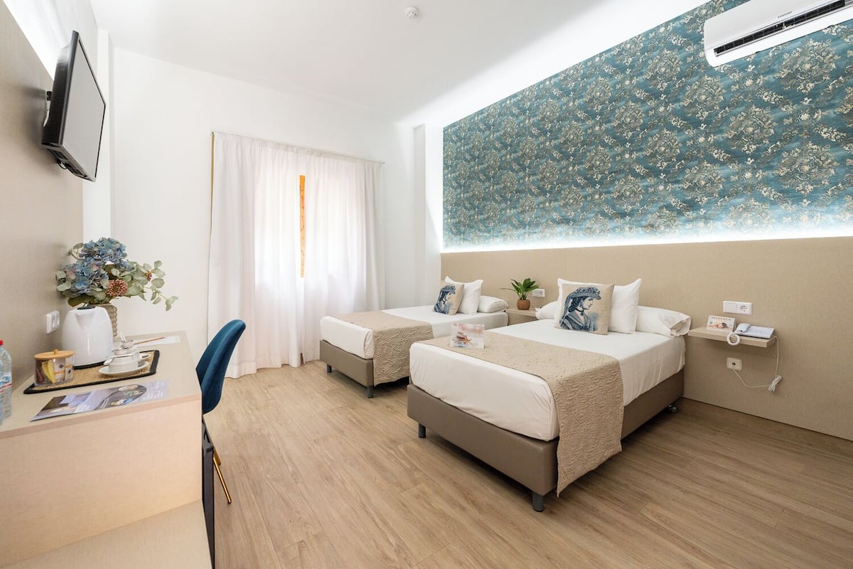 A hotel room with two beds, a desk, a chair, a TV, a massage service sign, and a large floral wall mural.