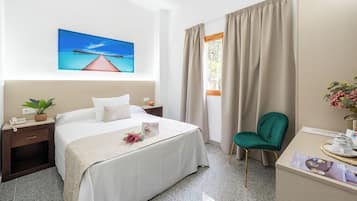 Habitación de hotel con cama, escritorio, silla, mesita de noche, teléfono, planta y un cuadro de un muelle.