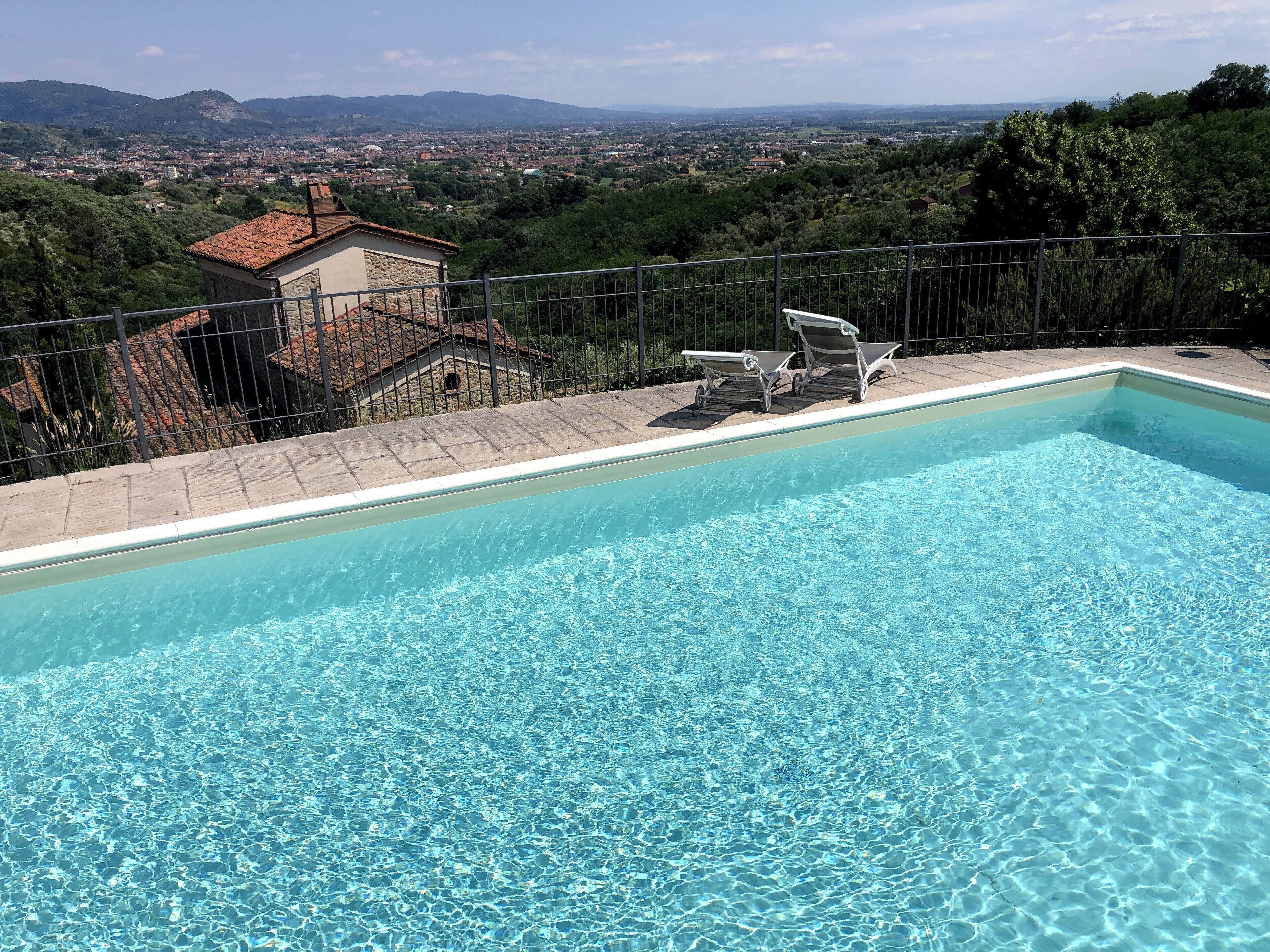 Piscina cristalina con vista a un pueblo y montañas al fondo.