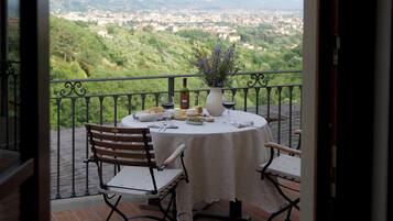 A balcony with a table set for two, overlooking a cityscape with hills.