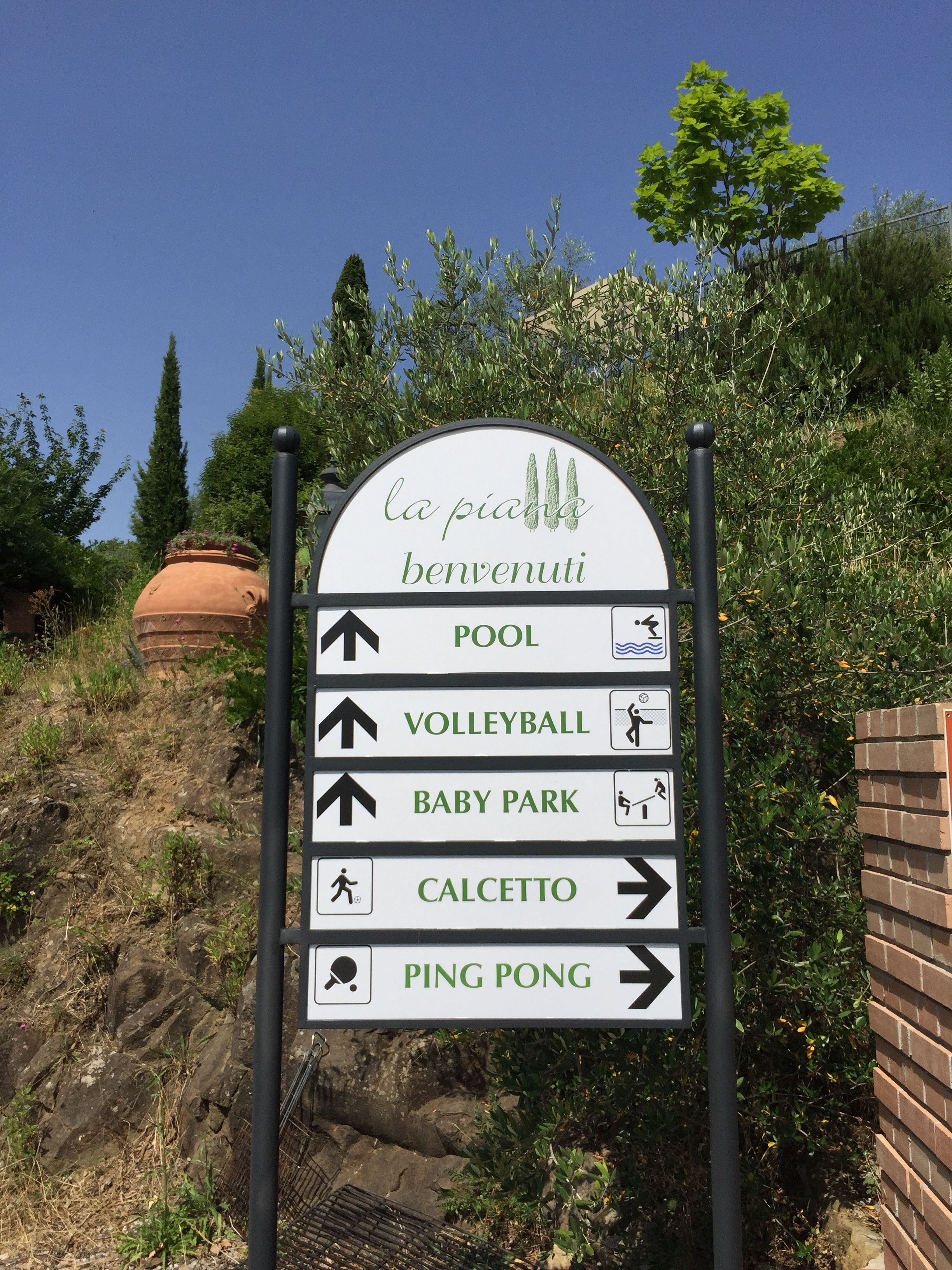 A directional sign with arrows pointing to various amenities including a pool, volleyball, baby park, caletto, and ping pong.