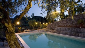 Una piscina con escalones de piedra y vistas a una colina con una torre.