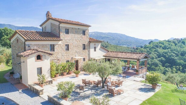 Una villa de piedra con patio, mobiliario exterior y vistas de las colinas circundantes.