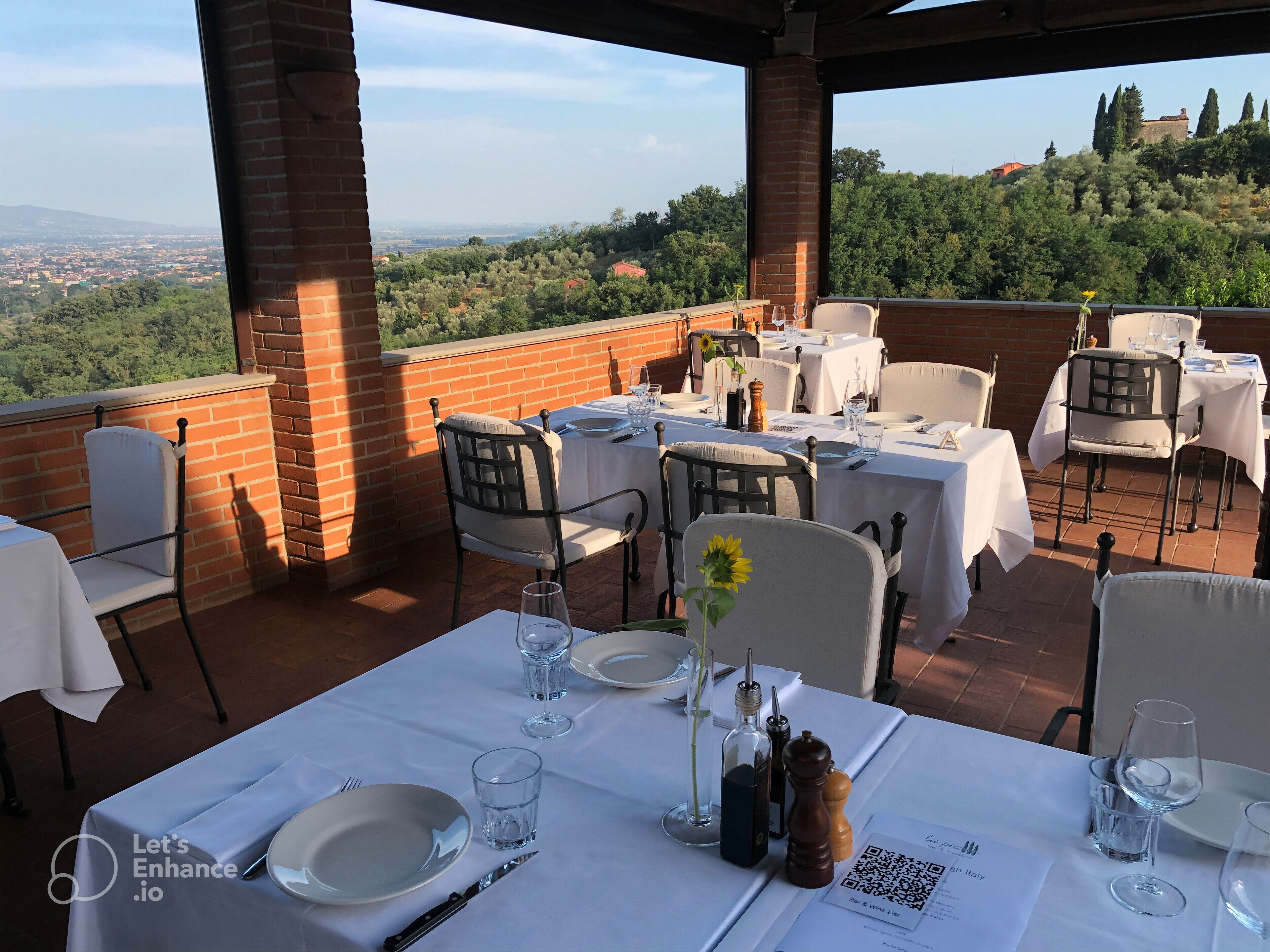 Eine Terrasse mit gedeckten Tischen mit Blick auf eine malerische Landschaft aus Bäumen und Hügeln.