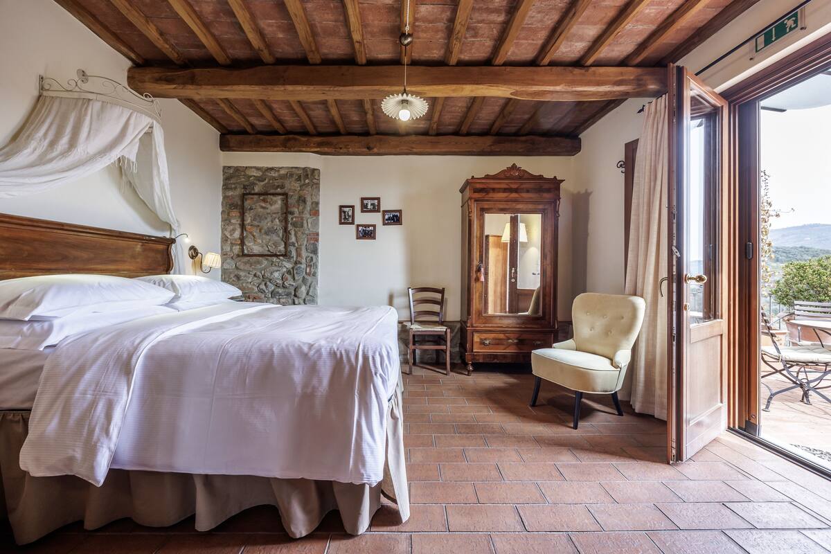 A bedroom with a bed, a chair, a mirror, and a stone wall.