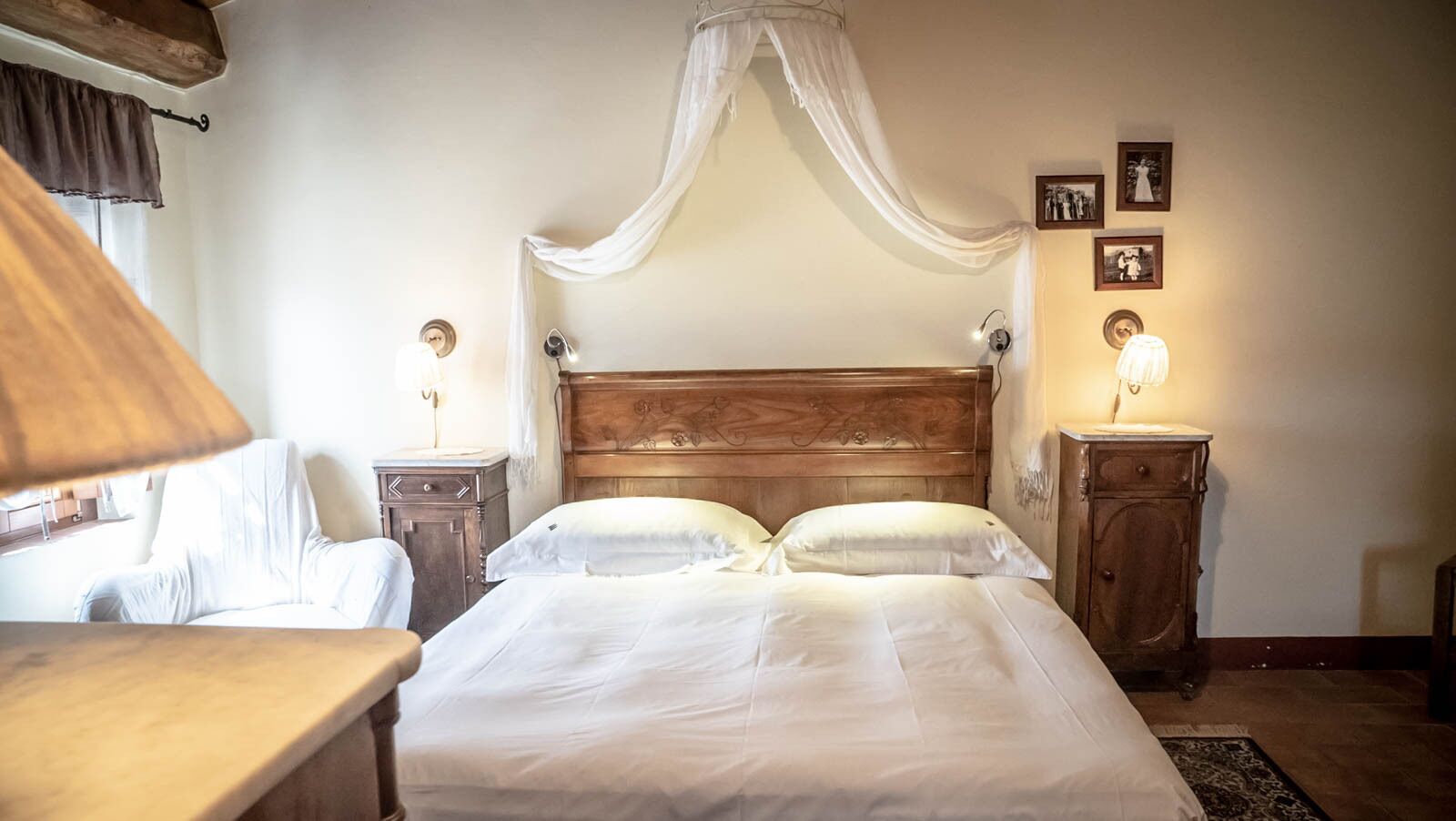 Un dormitorio con una cama grande, dos mesitas de noche, una mesita auxiliar y un cabecero de madera con dosel.