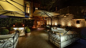 An outdoor patio area with a bed, a sofa, and a dining table under a large umbrella.