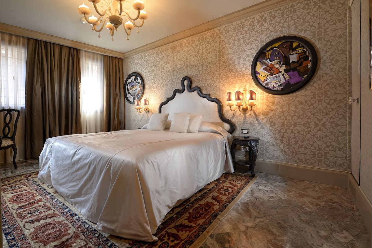 A neatly made bed with a white bedspread, a large patterned rug, and a chandelier above.