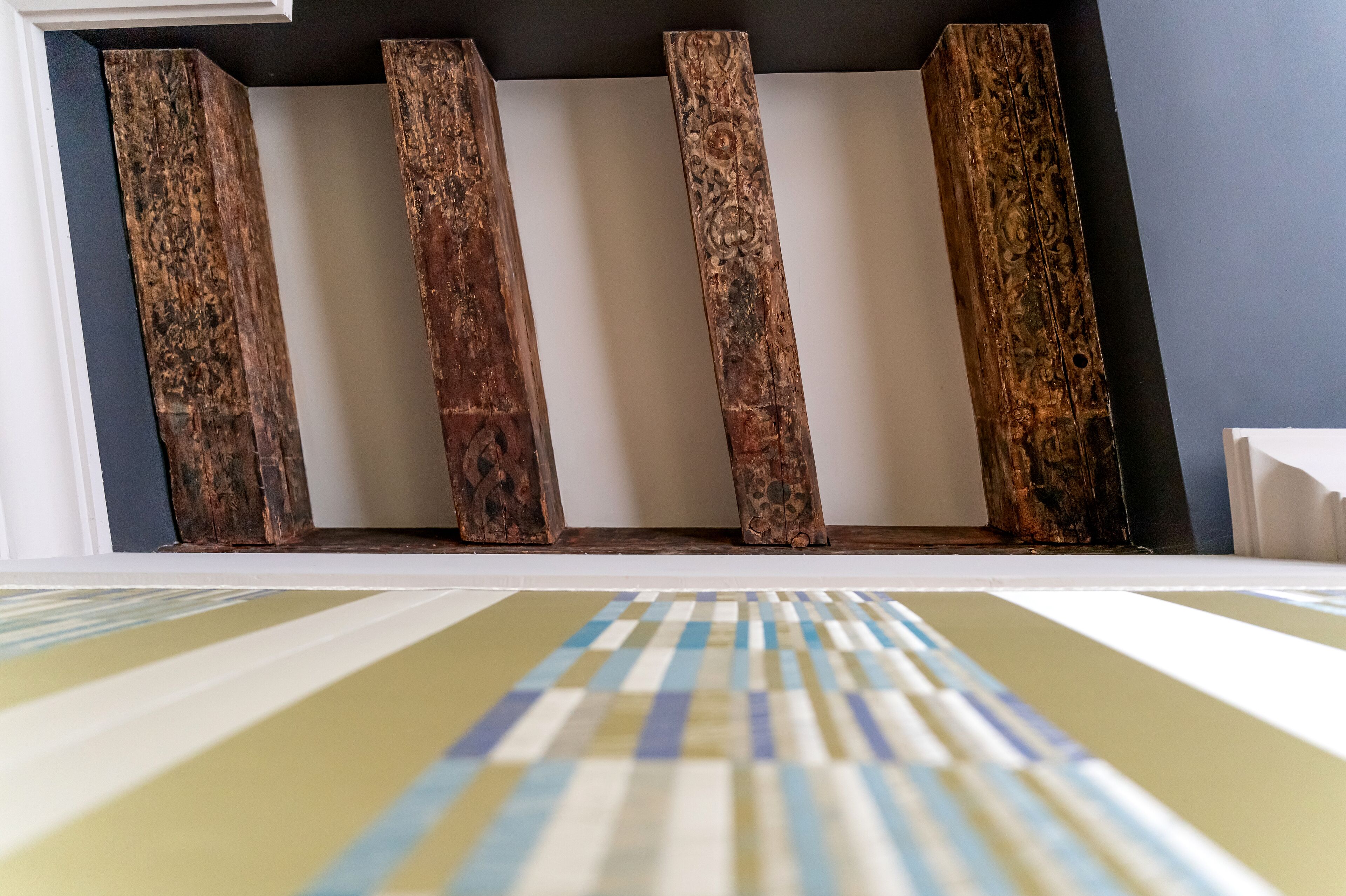 A room with a white wall and a wooden shelf with five vertical wooden planks.