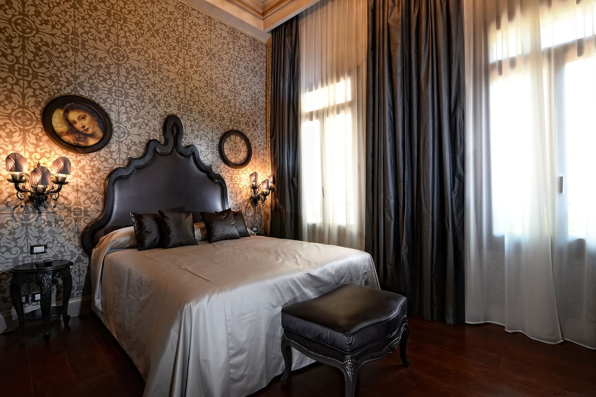 A neatly made bed with a headboard, a bedside table with a lamp, and a wall-mounted clock.