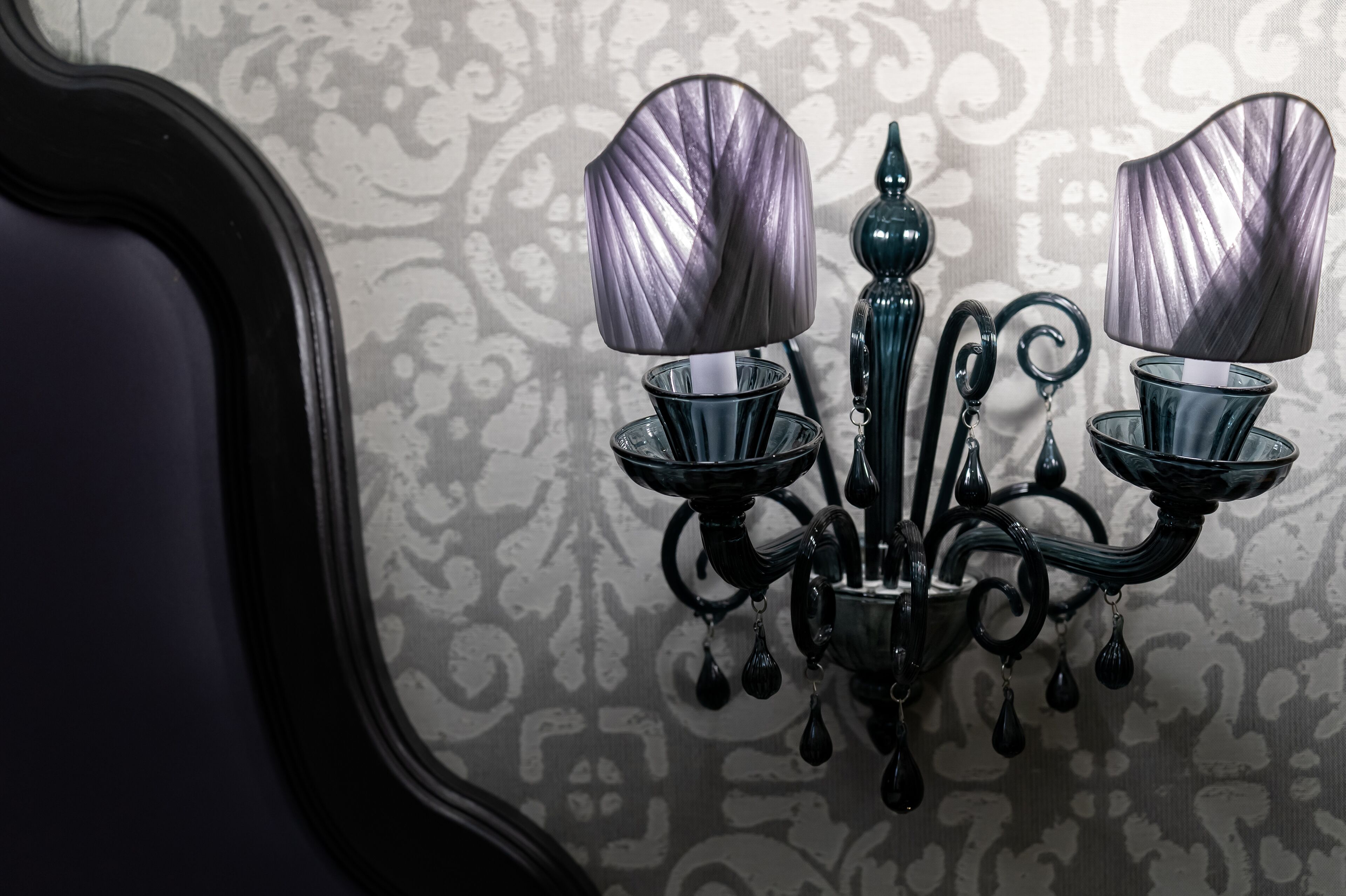 A black wall-mounted chandelier with two lampshades and a glass base.