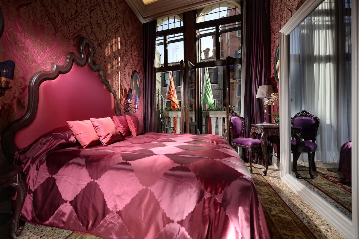 A room with a large bed, a window with curtains, and a view of the city.