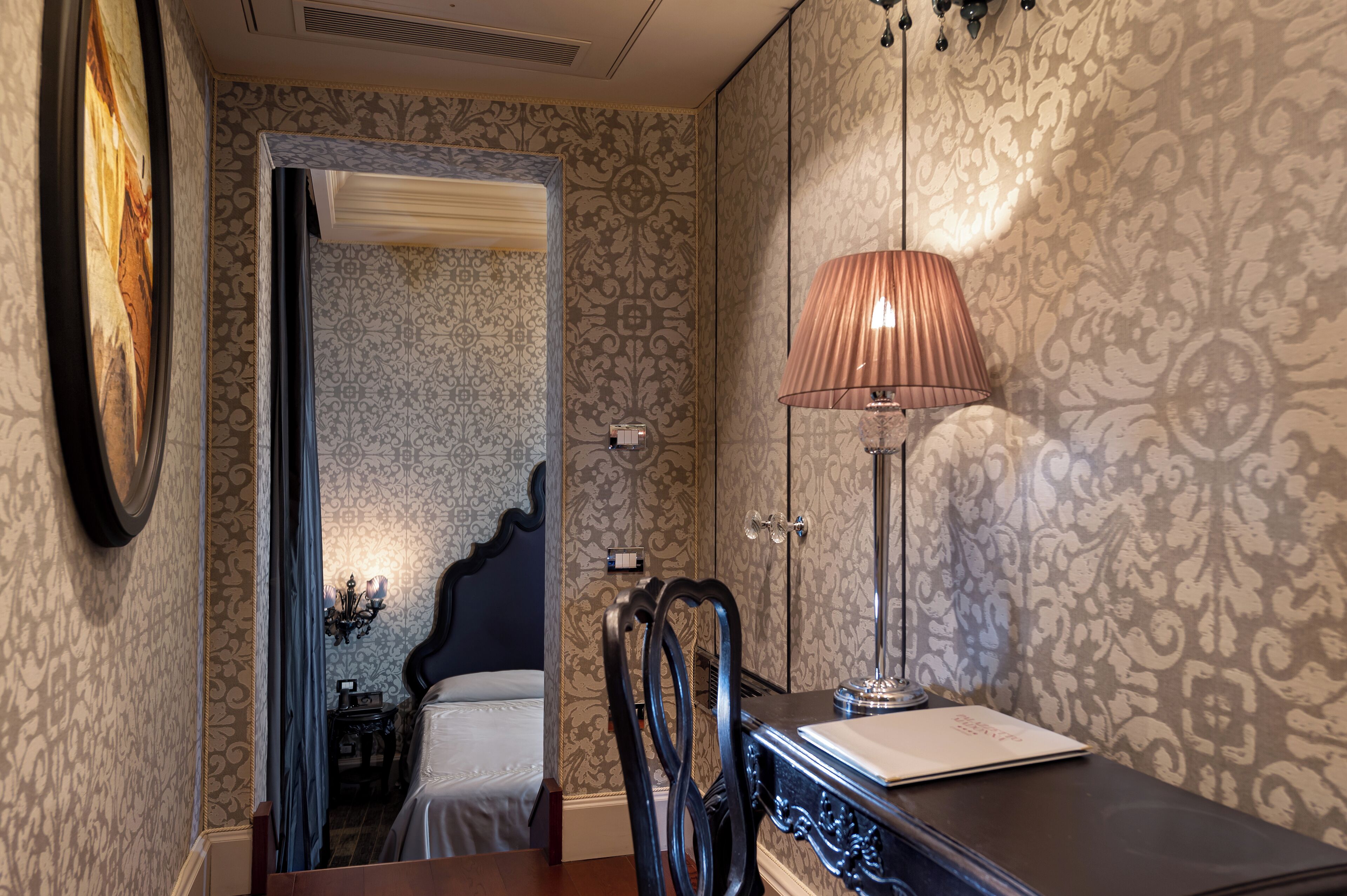 Et soveværelse med seng, skrivebord, lampe og stol.