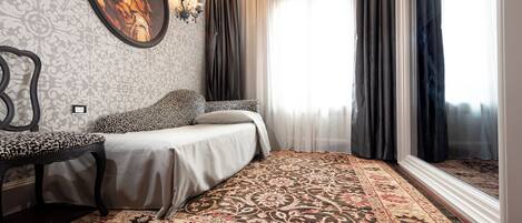Une chambre avec un tapis à motifs, un lit avec une tête de lit à motifs, un luminaire fixé au mur et une fenêtre avec des rideaux.