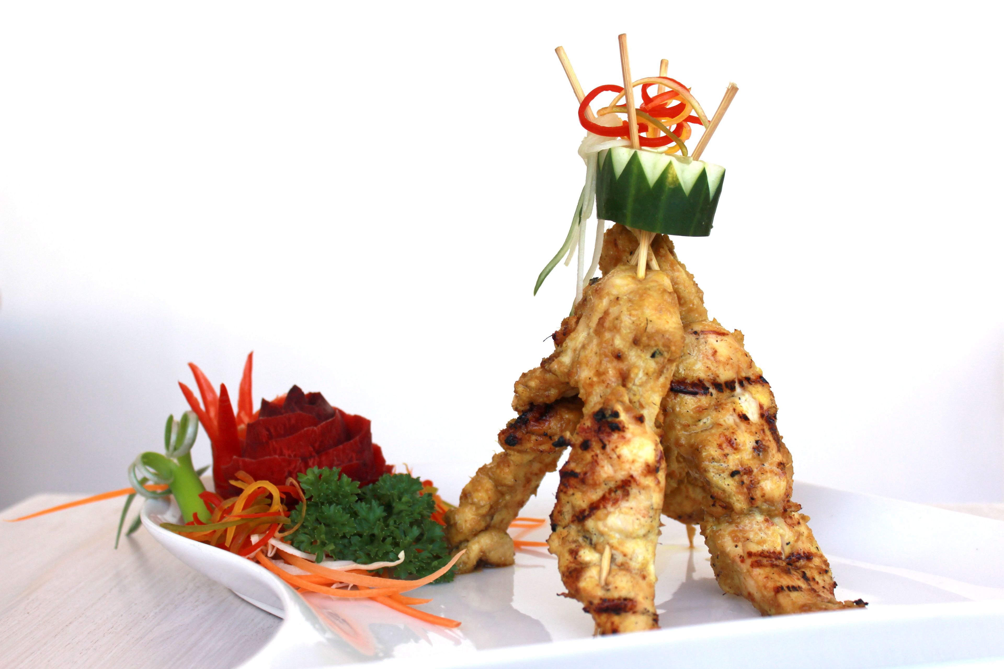 A plate with grilled meat skewers, garnished with carrot strips, red bell pepper, and parsley.