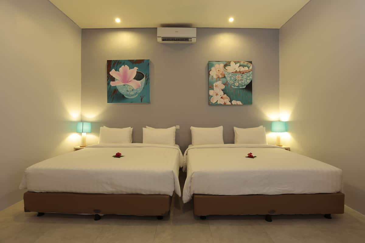 Cama doble con sábanas blancas y una rosa en cada una. Hay dos aires acondicionados y dos lámparas fijadas a la pared.