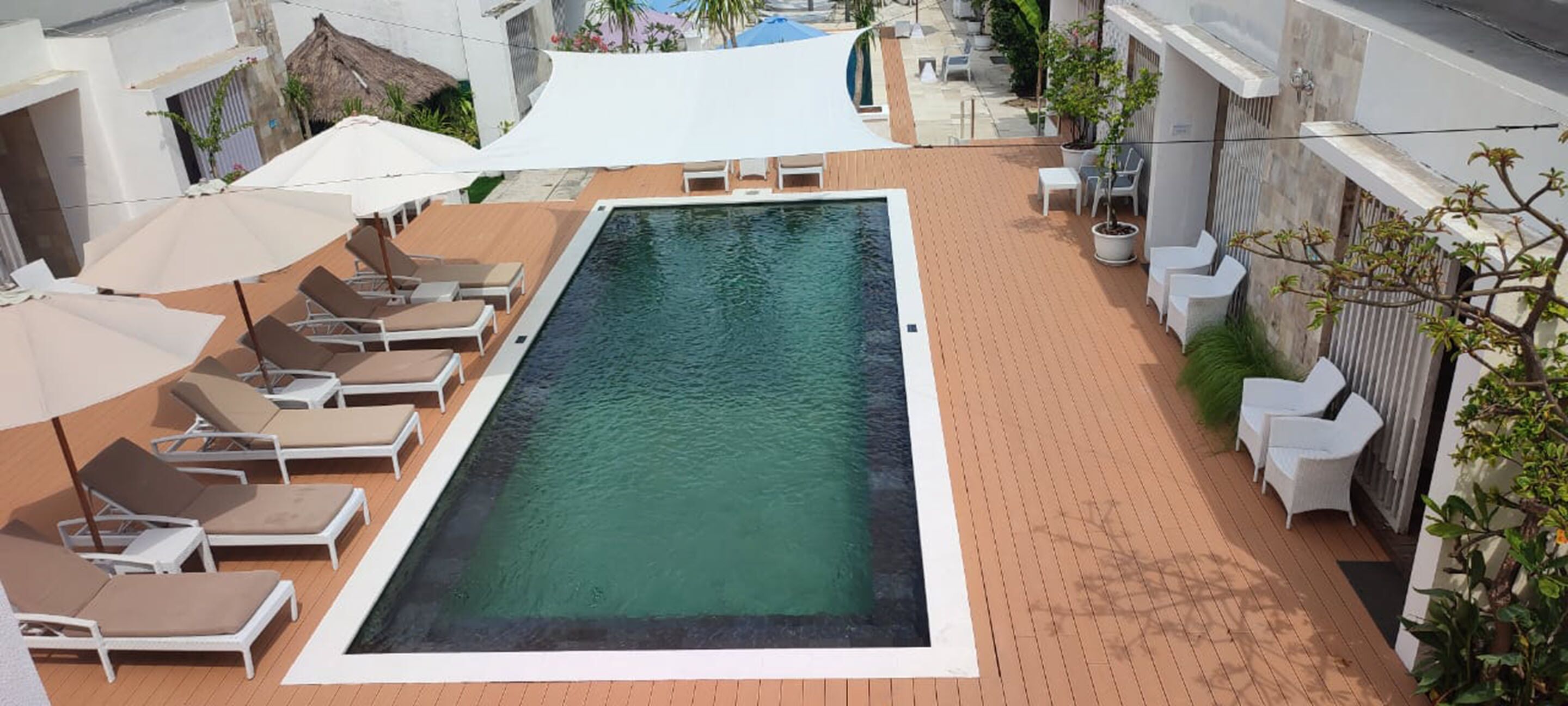 A rectangular swimming pool with lounge chairs and umbrellas on a tiled deck.