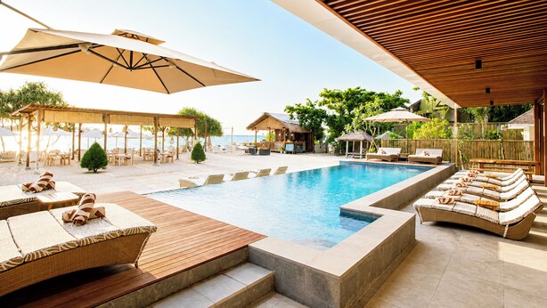 Un espace piscine aménagé avec des chaises longues, des parasols et une terrasse en bois.