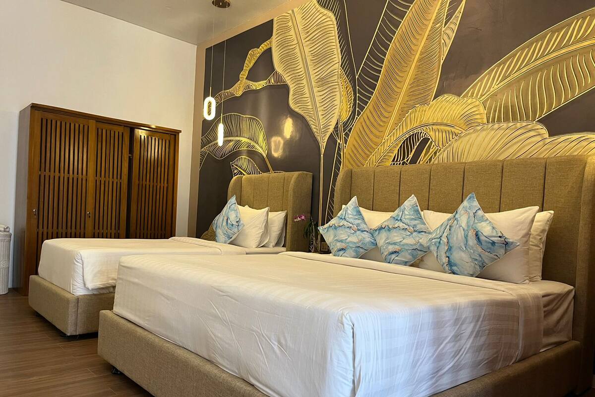 Una cama doble con cabecera, dos mesitas de noche y una pared con un diseño de hojas.