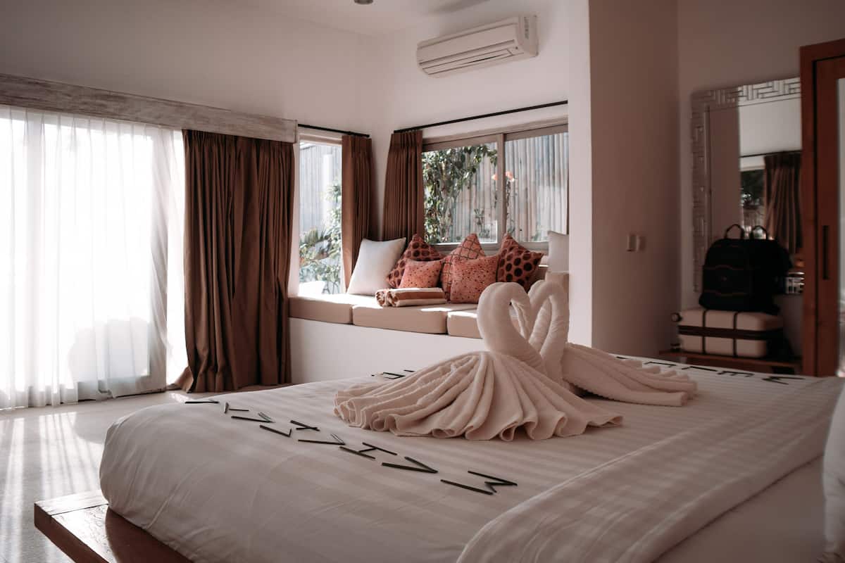 Un dormitorio con una cama grande, una ventana con cortinas, un sofá con cojines y un espejo.