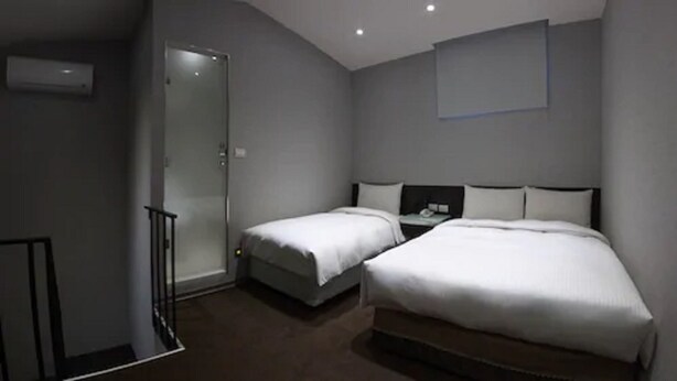 A modern hotel room with two single beds, a small bedside table with a lamp, a built-in shelf, and a sliding door leading to a bathroom. - Chingjing Inn (Taipei)
