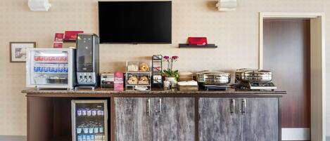 Een receptiegedeelte met een koelkast, een koffieapparaat, een flatscreen-tv en een kleine koelkast met drankjes.