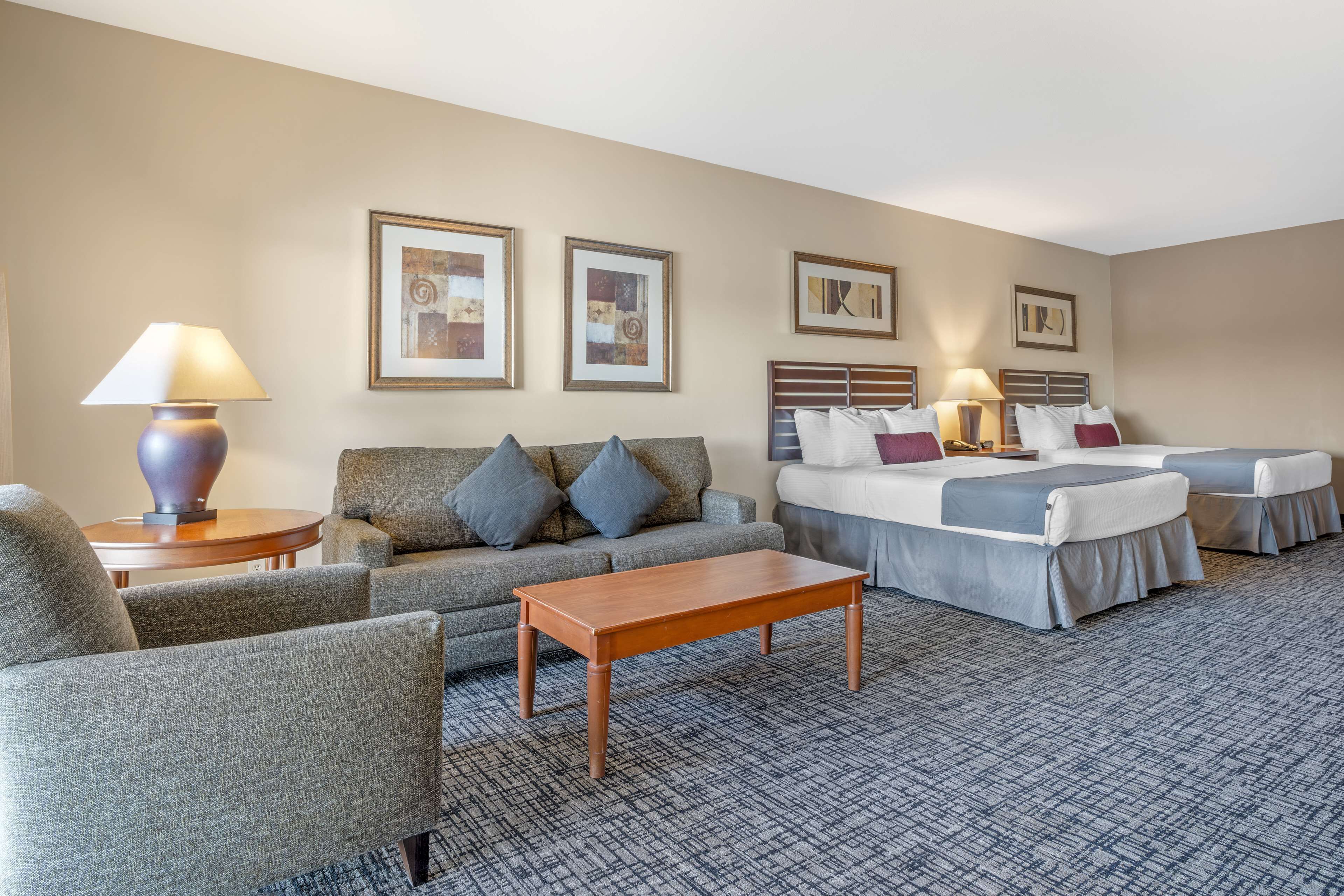 Une chambre d’hôtel avec un canapé, deux lits, une table basse et des œuvres d’art encadrées accrochées aux murs.