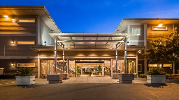 Una entrada de hotel moderna con un paseo techado, puertas de cristal y una escalera que lleva al vestíbulo.