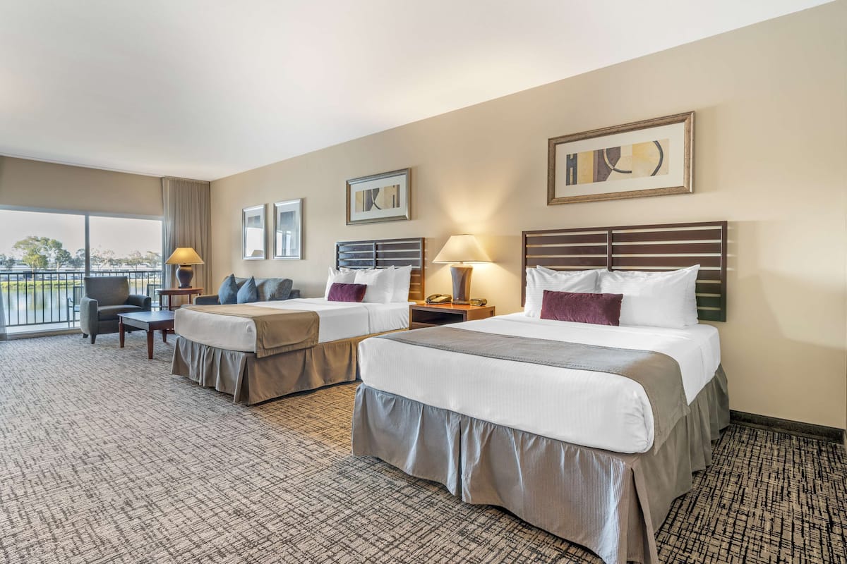 A hotel room with two beds, a sofa, a desk, and a balcony with a view.