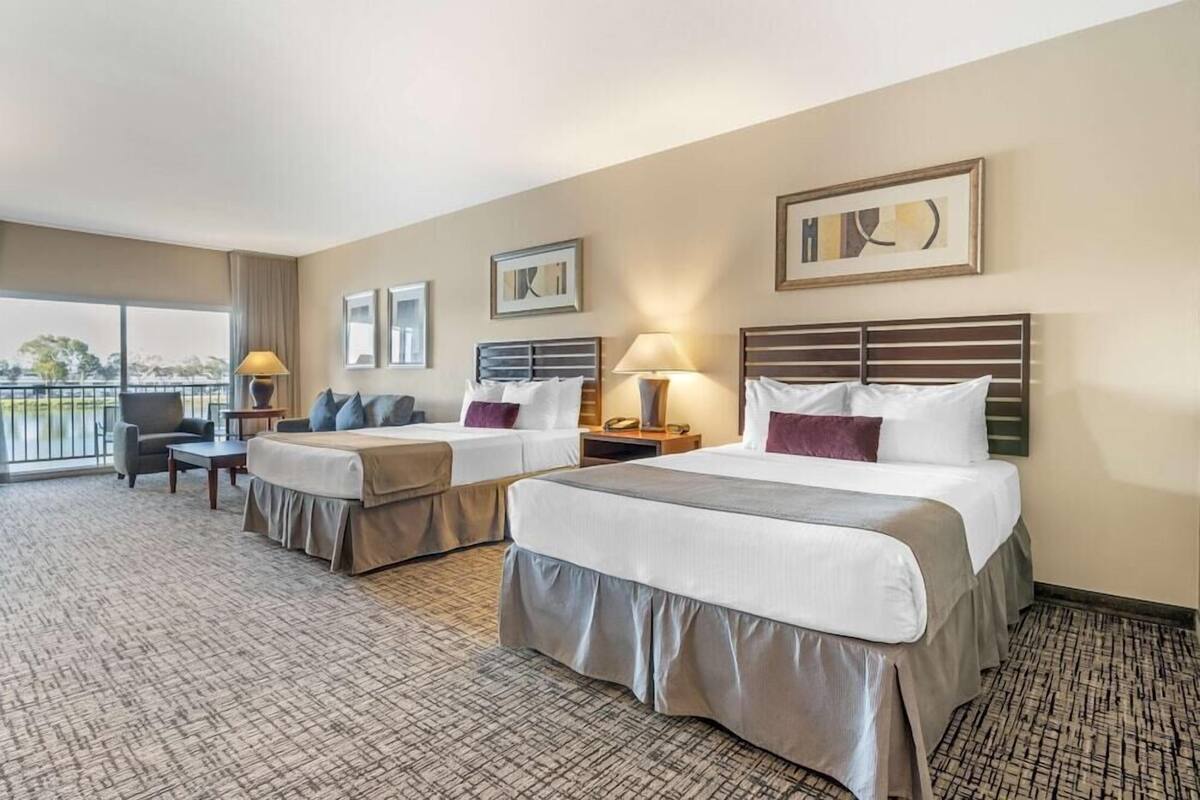 Habitación de hotel con dos camas, un balcón y vistas al exterior.
