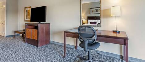 Habitación de hotel con escritorio, silla, televisor, lámpara y espejo.