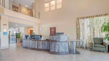 Eine geräumige Lobby mit einer Rezeption, einer Sitzecke und einer Treppe zu einer oberen Ebene.