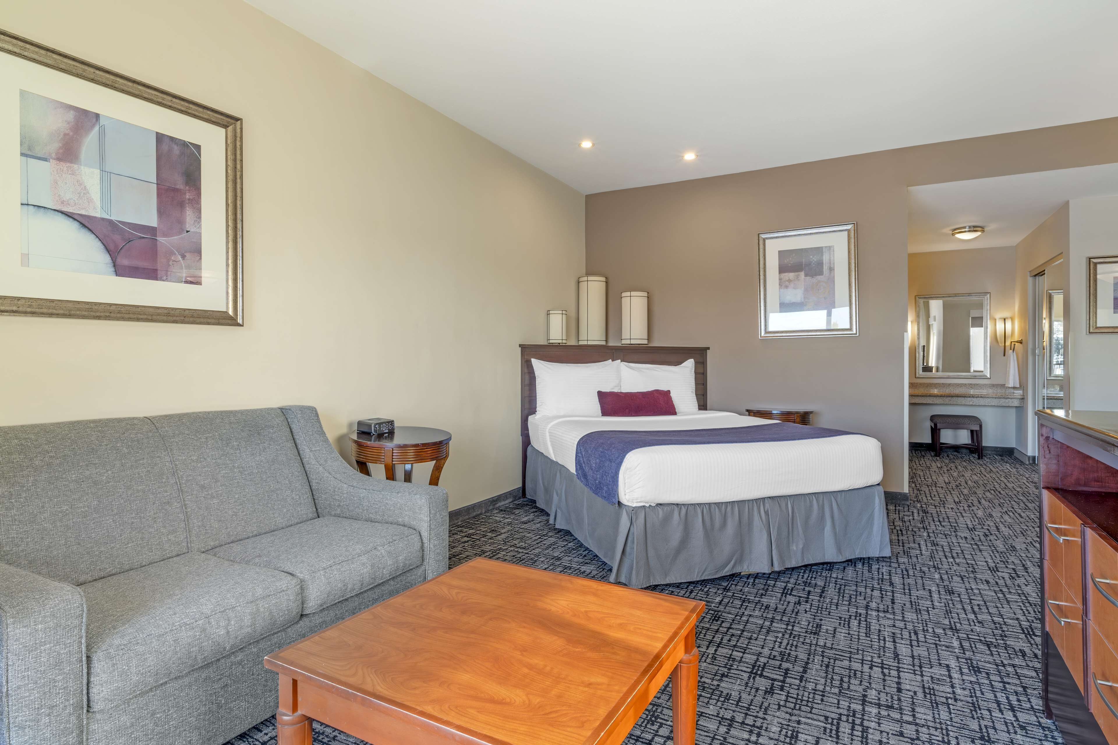A hotel room with a bed, a gray sofa, a wooden table, and a carpeted floor.