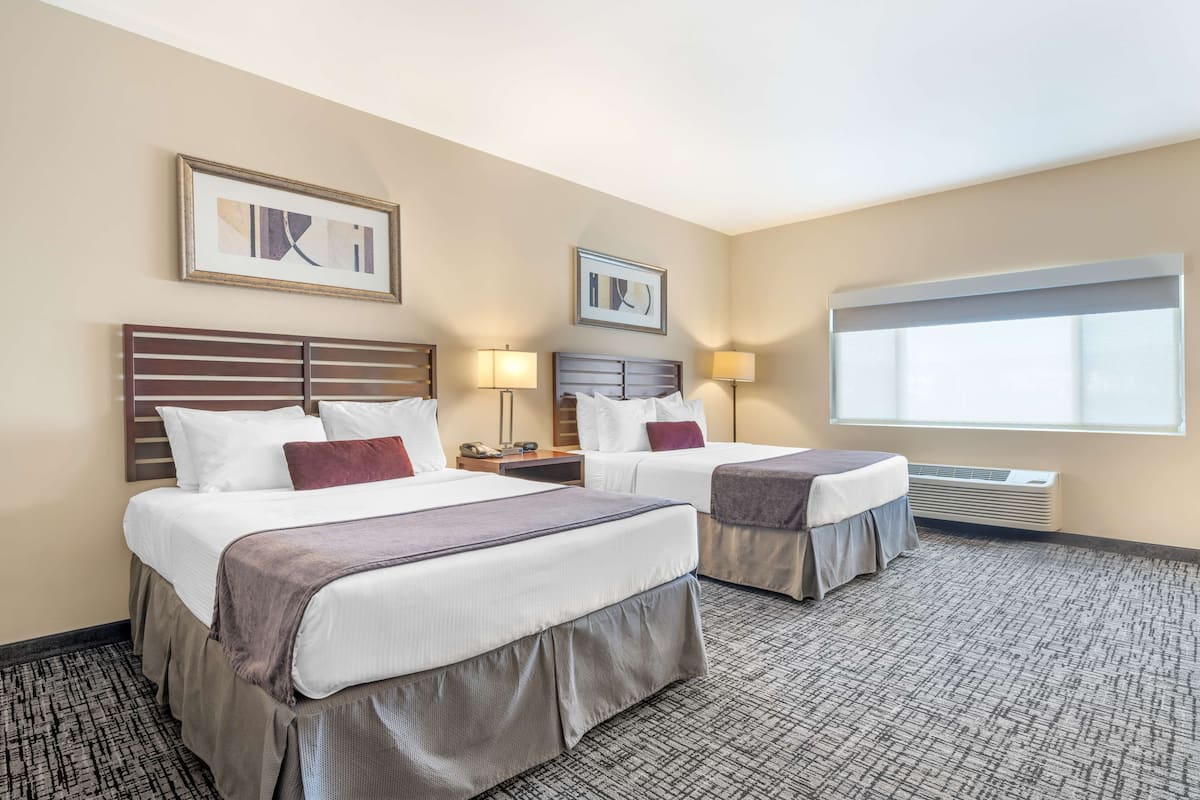 A hotel room with two beds, a large window, and a wall-mounted air conditioner.