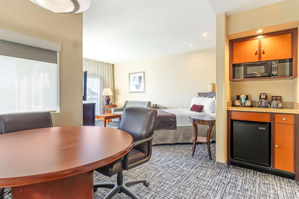 A hotel room with a conference table, a bed, a desk, a lamp, a microwave, and a refrigerator.