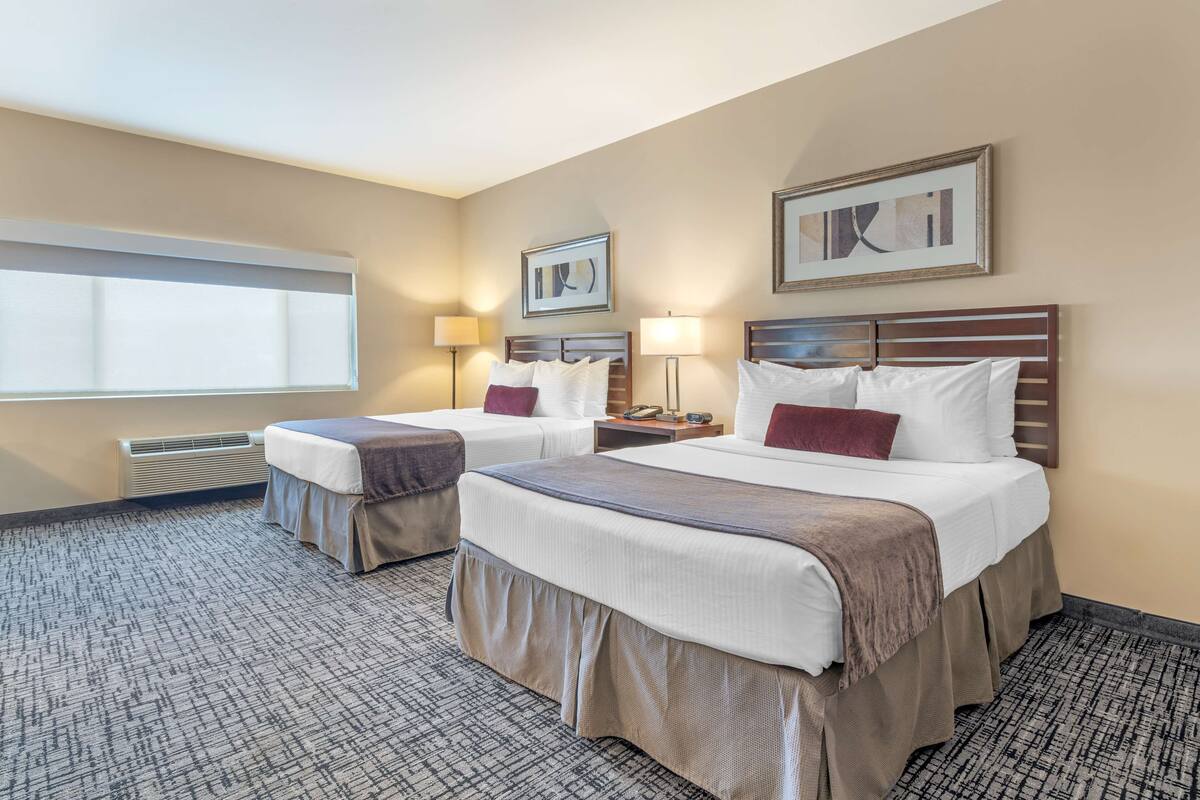 A hotel room with two beds, a large window, and a wall-mounted artwork.