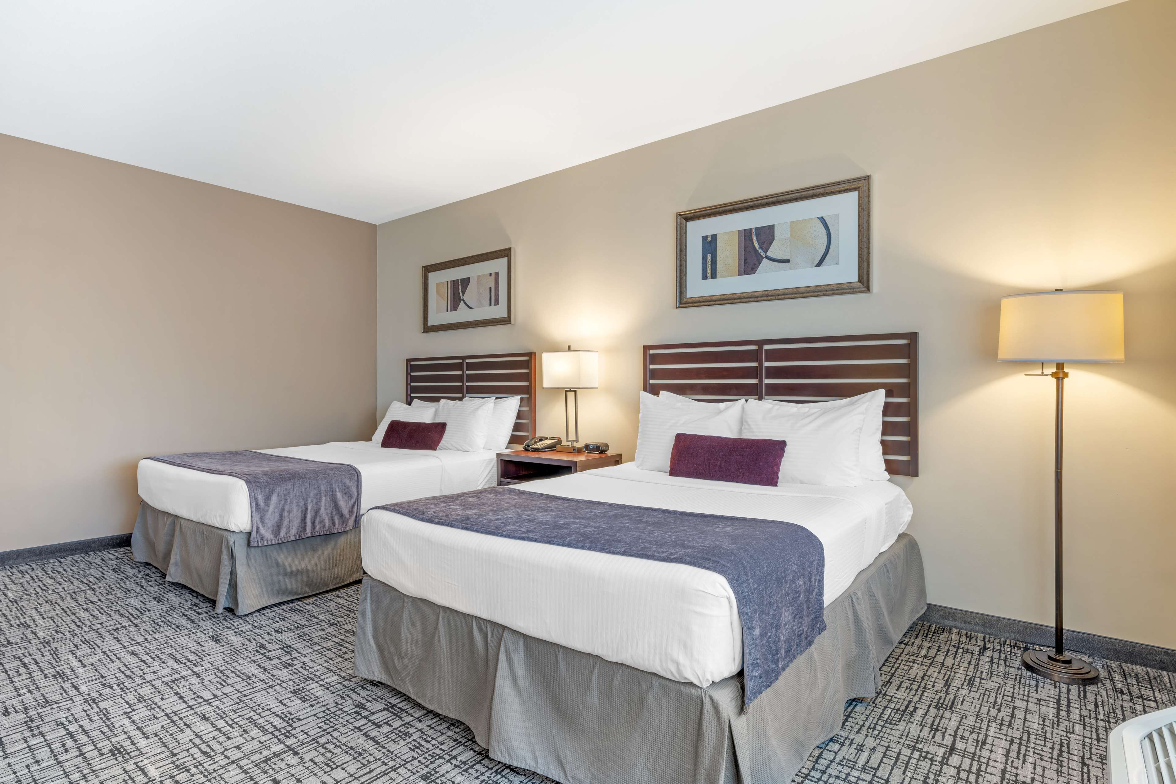 A hotel room with two beds, a nightstand, a lamp, and artwork on the walls.