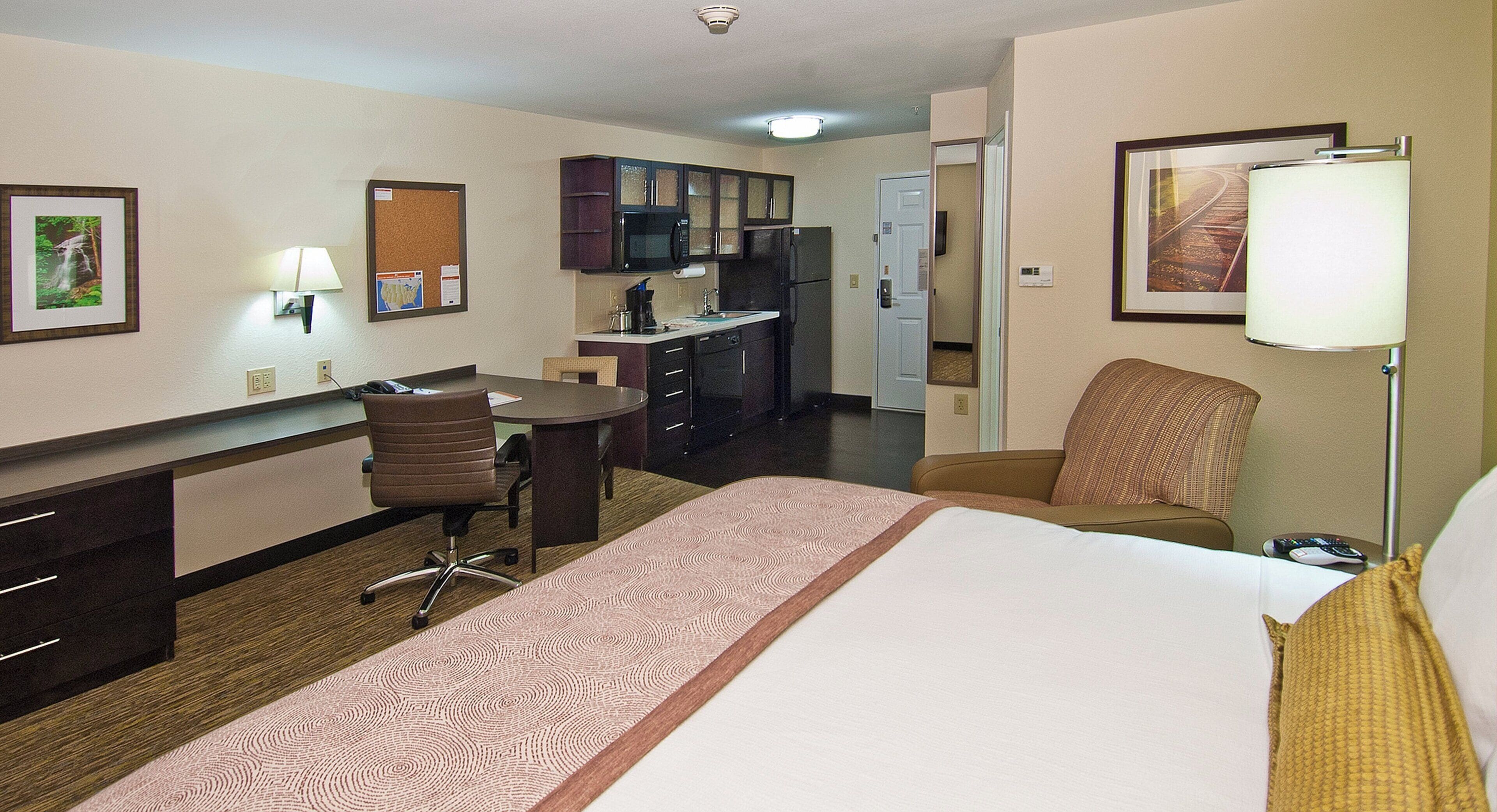 Habitación de hotel con cama, escritorio, silla, microondas, refrigerador y puerta que da a un baño.