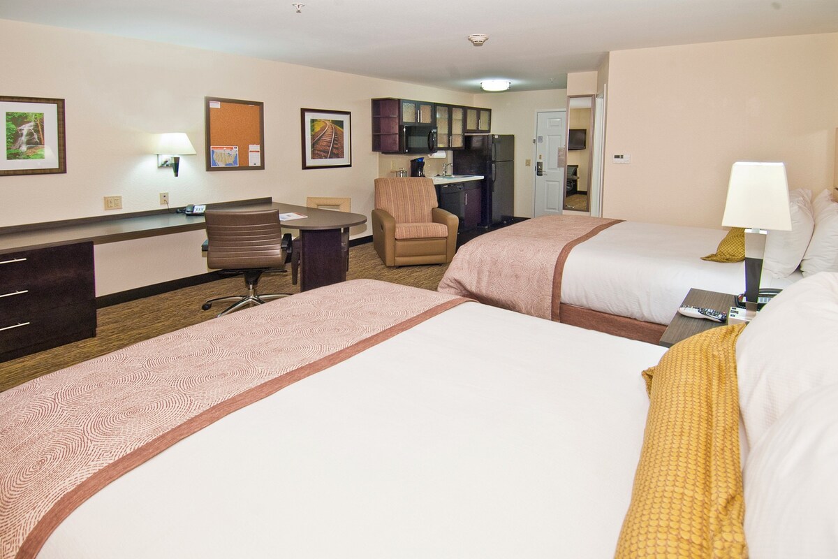 Une chambre d’hôtel avec deux lits, un bureau, une chaise, un coin cuisine et une salle de bain.